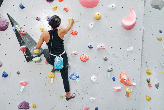 Fit young female athlete moving up on steep rock, climbing on artificial wall indoors. Extreme sports and bouldering concept