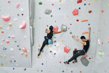 Strong young couple training in bouldering facility, they are climbing on artificial wall indoors - obrazy, fototapety, plakaty