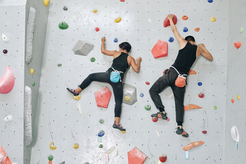 Sportswoman and sportsman with magnesium powder bags climbing up the bouldering wall, view from the...