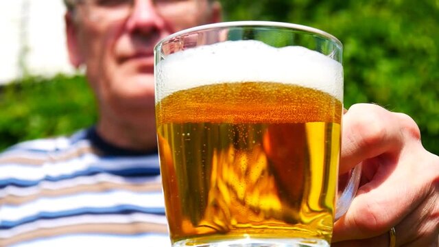 Close-up of a glass mug with a beer in the hand of an elderly man who then drinks it