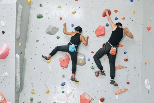 Sportswoman and sportsman with magnesium powder bags climbing up the bouldering wall, view from the back
