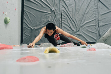 Strong athletic man bouldering at indoor climbing center without auto belay devices