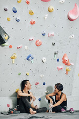 Team of cheerful barefoot climbers sitting at bouldering wall, drinking water and talking after...