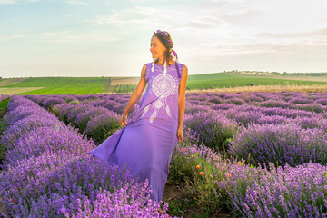 girl in a purple dress with a wreath and ribbons on her head in a lavender field at sunset. Boho style
