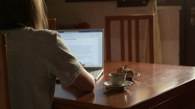 4k a girl working with laptop in the kitchen, cessing a work, taking a cup of coffee to break. Domestic life, remote work and study at home, online learning, smartworking