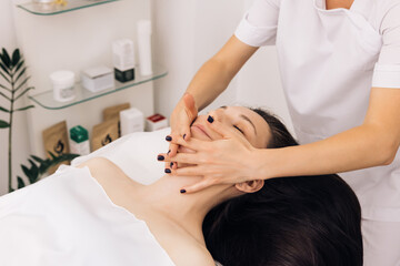 Fototapeta na wymiar Face Massage in beauty spa salon. Caucasian woman receiving a facial massage at an aesthetic salon. Spa facial Massage. Body care, skin care, wellness, wellbeing, beauty treatment concept