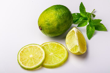 whole lime and lime slices with mint leaves on white background