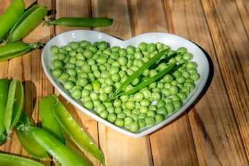 Green peas on a white plate in the shape of a heart.