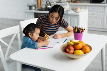 Asian mother drawing with child near fruits on table