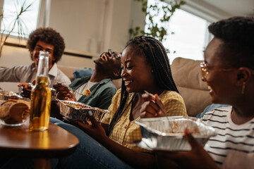 Group of young friends enjoying takeout food at home during weekend