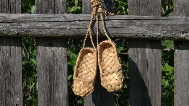 Rustic rural concept. Antique handmade rustic shoes - bast shoes. A pair of bast shoes hanging on a wooden fence.