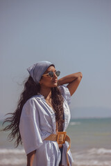 A black girl strolling on the beach cheerful and smiling as she looks to the right with sunglasses...