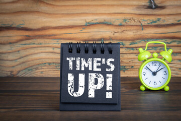 Time's Up! Black notebook and green alarm clock on a wooden background