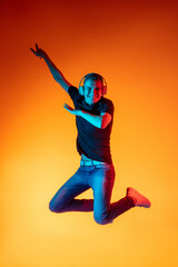 Fototapeta na wymiar Portrait of young Caucasian man in casual clothes isolated over gradient red orange studio background in neon light with copyspace for ad. Concept of human emotions