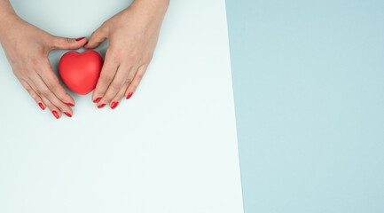 emale hands holds red heart, blue background. Love and donation concept, copy space