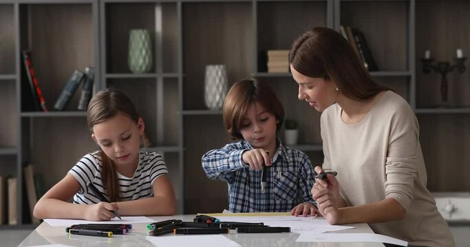 Caring young mother spend free time with little adorable son and daughter draw together with color felt pens in cozy living room. Babysitting daycare, children development and favourite hobby concept