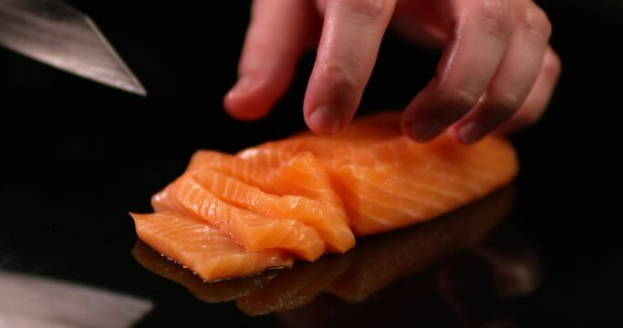 Chef male hands cutting raw salmon on a black surface. Close up view shot on RED camera.