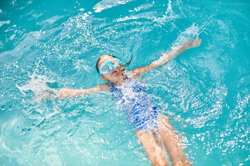 Little girl in goggles having fun, dives and swim in the swimming pool