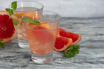 Cocktail with grapefruit on a light background with a sprig of mint and ice cubes.