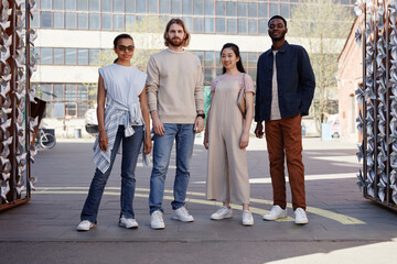 Full length portrait of diverse group of young people standing in city setting and looking at camera