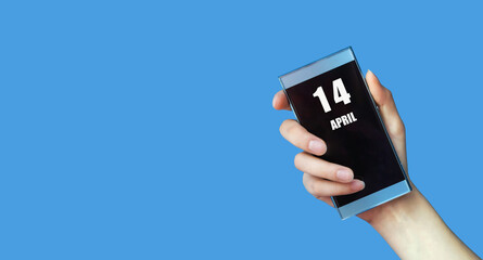 April 14. 14th day of the month, calendar date.Woman's hand holds mobile phone with blank screen on blue isolated background.Spring month, day of the year concept