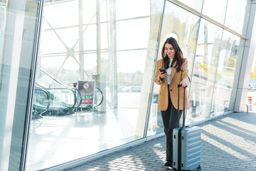 Businesswoman on commute transit typing on the smartphone while walking with hand luggage in a...