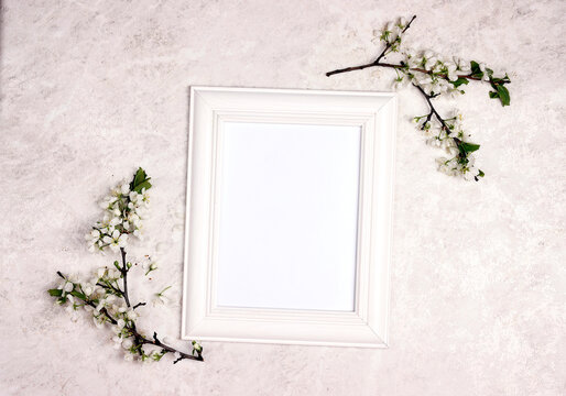 Empty white frame with apple blossom branches on light marble background.