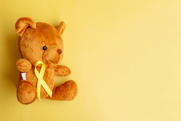 Yellow Ribbon with Bear doll on yellow color background for supporting kid living and illness. September Childhood Cancer Awareness month and World cancer day concept