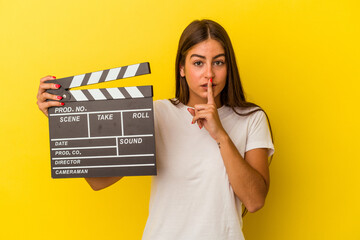 Young caucasian woman holding clapperboard isolated on white background keeping a secret or asking for silence.