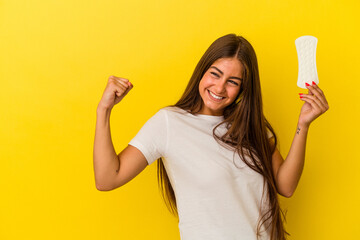 Young caucasian woman holding a compress isolated on yellow background raising fist after a...