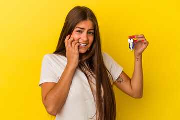 Young caucasian woman holding a home keys isolated on yellow background biting fingernails, nervous...