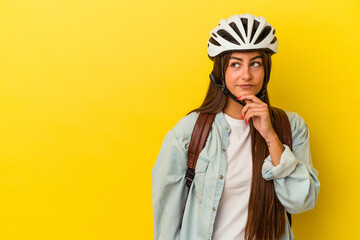 Young student caucasian woman wearing a bike helmet isolated on yellow background looking sideways with doubtful and skeptical expression.