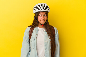 Young student caucasian woman wearing a bike helmet isolated on yellow background confused, feels doubtful and unsure.