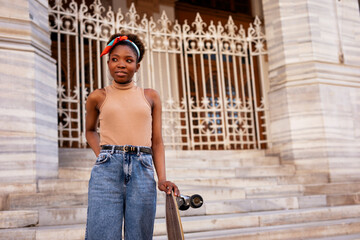 Portrait of happy african-american woman with skateboard. Young stylish woman with skateboard outdoors..