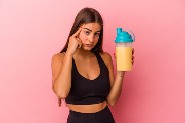 Young caucasian woman holding a protein shake isolated on yellow background pointing temple with finger, thinking, focused on a task.