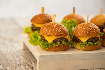 mini burgers with cheese and lettuce with sticks on a wooden background - obrazy, fototapety, plakaty