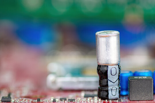 Closeup view of a blown capacitor on a circuit board. The metal inside has blown up through the top. No brand markings. Shallow depth of field.