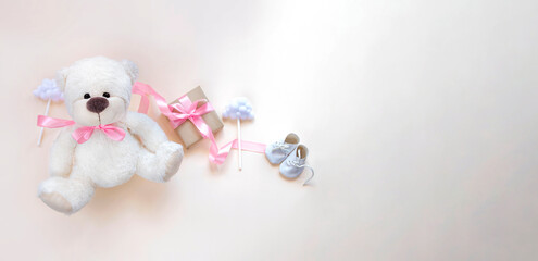 White teddy bear, present with pink silk ribbon, tiny clouds and baby shoes on pale background. Baby shower, party invitation concept