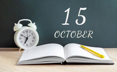 october 15. 15-th day of the month, calendar date.A white alarm clock, an open notebook with blank pages, and a yellow pencil lie on the table.Autumn month, day of the year concept