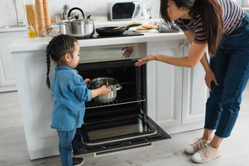 Mother pointing at oven near asian kid with pan