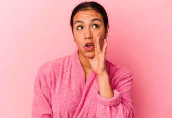 Young Venezuelan woman wearing a bathrobe isolated on pink background is saying a secret hot braking news and looking aside