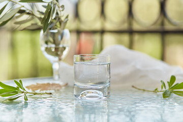 Glass of fresh water. Decorative green leaves and branch of an olive tree in a glass. Glyph of Purification. Water - symbol of life. Copy space