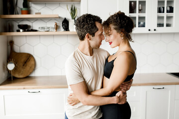 Happy millennial husband and wife hug cuddle and enjoy romantic moment in modern kitchen, loving young couple embrace at home, look each other in eyes, having romance together, relationships concept