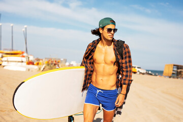 Portrait of handsome surfer with his surfboard. Young man with a surfboard on the beach.