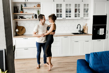 Happy Caucasian couple in sportswear smiling dancing or doing sport exercises together in modern kitchen at home during quarantine. Happy couple spend time together happily, relationship concept