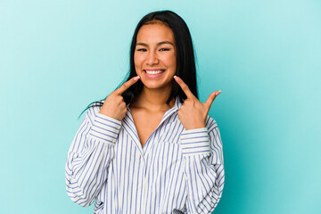 Young Venezuelan woman isolated on blue background smiles, pointing fingers at mouth.