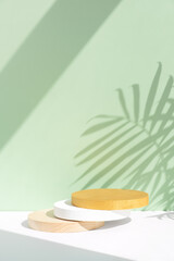 Fototapeta na wymiar Wooden, white and gold scenes on a white table on a pastel green background with a shadow of palm leaves. Premium podium for advertising your product. Background for the product presentation.