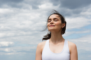 young pleased woman in crop top against blue sky with clouds