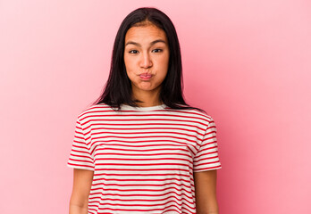 Young Venezuelan woman isolated on pink background blows cheeks, has tired expression. Facial...