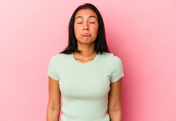Young Venezuelan woman isolated on pink background shrugs shoulders and open eyes confused.